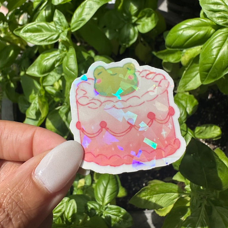 A die-cut sticker featuring a cute pink frog themed cake sticker , set against a background of a cozy garden. Stickers for water bottle, laptop sticker, cute sticker, cool sticker 