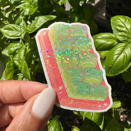 A cute die-cut sticker featuring a green frog bread set against a cozy background of green basil plants. Stickers for water bottle, laptop sticker, cute sticker, cool sticker 