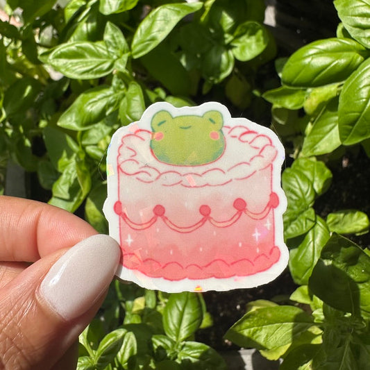 A die-cut sticker featuring a cute pink frog themed cake sticker , set against a background of a cozy garden. Stickers for water bottle, laptop sticker, cute sticker, cool sticker 
